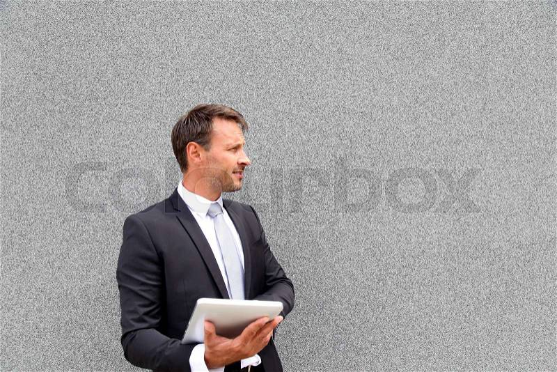 Businessman using electronic tablet leant against wall, stock photo