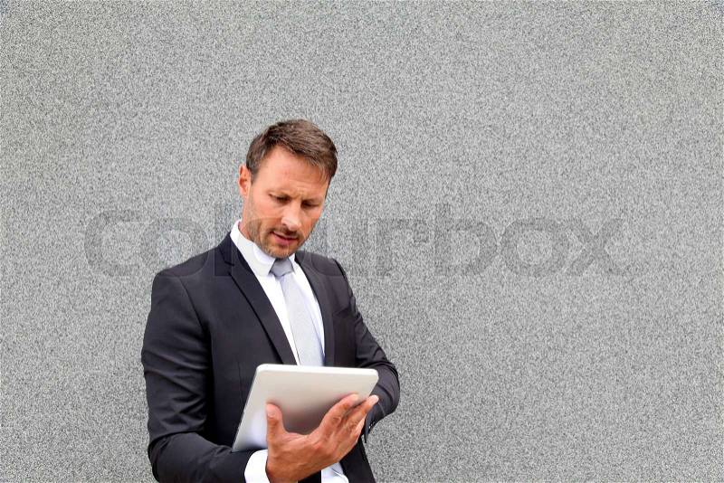 Businessman using electronic tablet leant against wall, stock photo