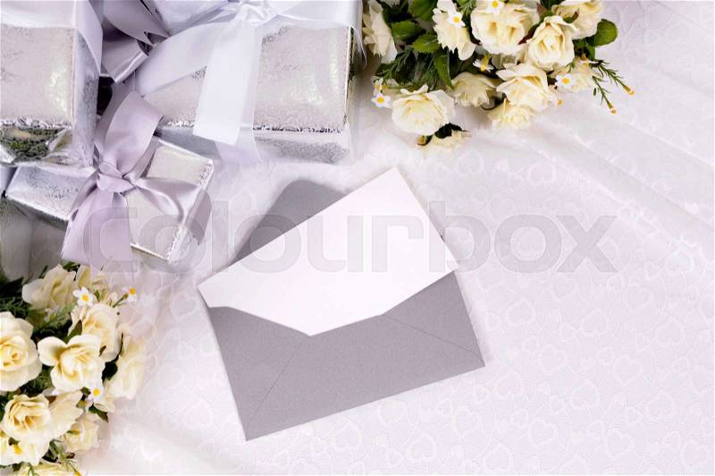Blank invitation or thank you card with several wedding gifts and white rose bouquet laid on bridal lace. Space for copy, stock photo