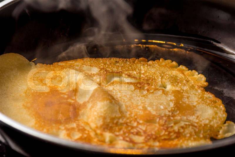 Fresh golden pancake or crepe baking in a pan, stock photo