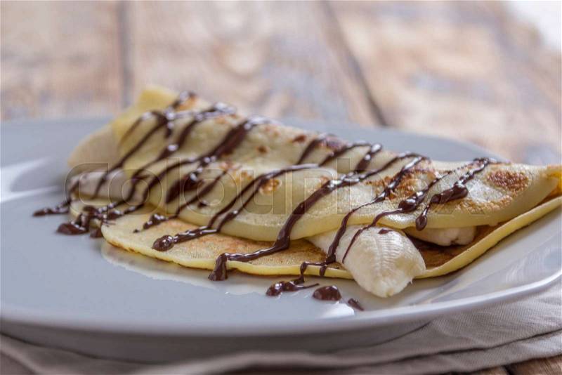 Crepe filled with banana and chocolate sauce topping on a rustic wooden plate, stock photo