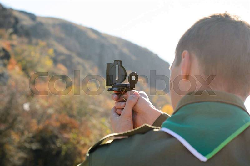 Rear View of a Boy Scout Navigating in the Wilderness While Taking a Reading on a Mountain with his Magnetic Compass Device, stock photo