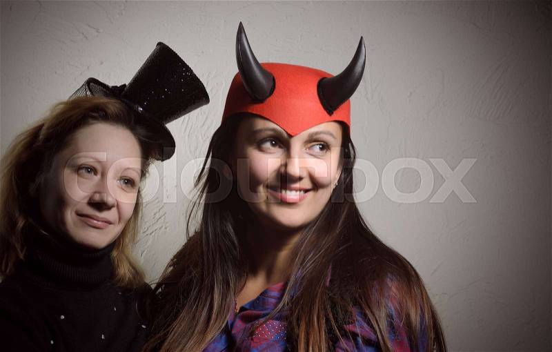 Two Smiling Women Wearing Top and Devil Hats Looking at the Right Frame on a Gray Gradient Background, stock photo