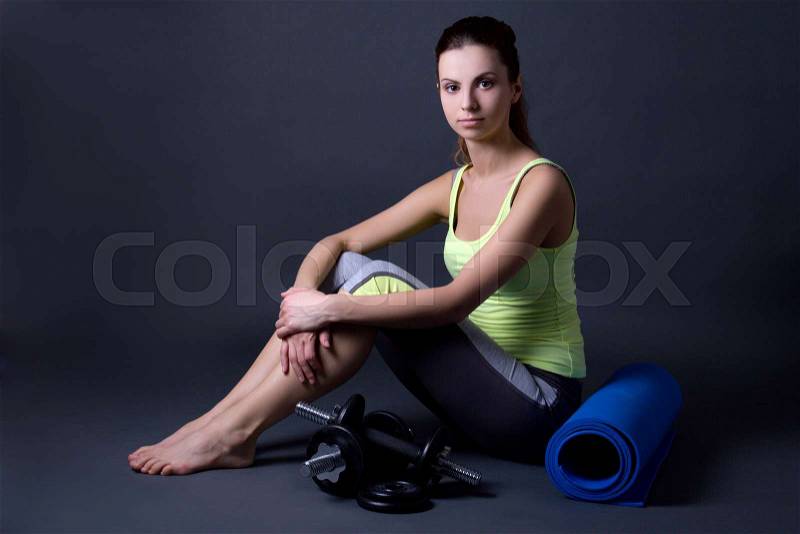 Young woman in sports wear with yoga mat and dumbbells over grey background, stock photo