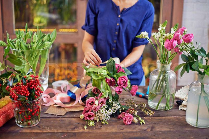 Female florist tying flowers up with decorative ribbon at workplace, stock photo