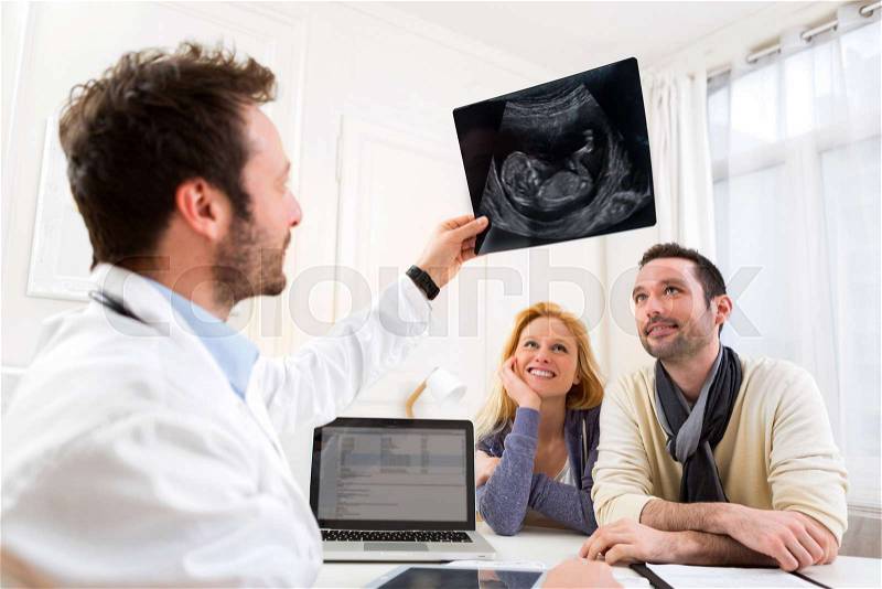 View of a Doctor shows an ultrasound to a young happy couple, stock photo