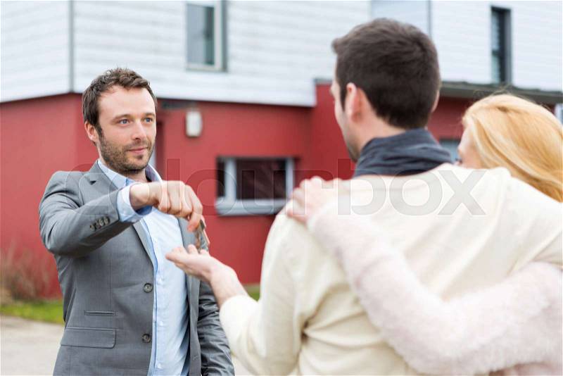 View of a Real estate agent delivers keys to young atractive couple, stock photo