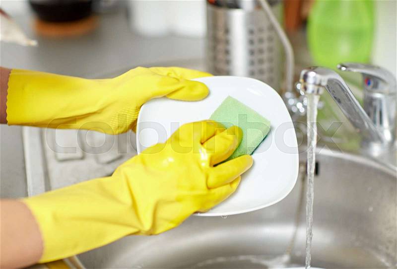 People, housework, washing-up and housekeeping concept - close up of woman hands in protective gloves washing dishes with sponge at home kitchen, stock photo