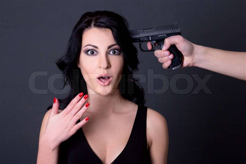 Young beautiful terrified woman hostage and male hand with gun over grey background, stock photo