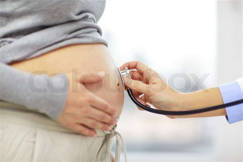 Pregnancy, healthcare, people and medicine concept - close up of pregnant woman belly and doctor hand with stethoscope at medical appointment in hospital, stock photo