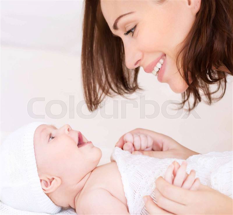 Closeup portrait of beautiful cheerful mother playing with cute little baby lying down on the bed, loving young family, happy motherhood concept, stock photo