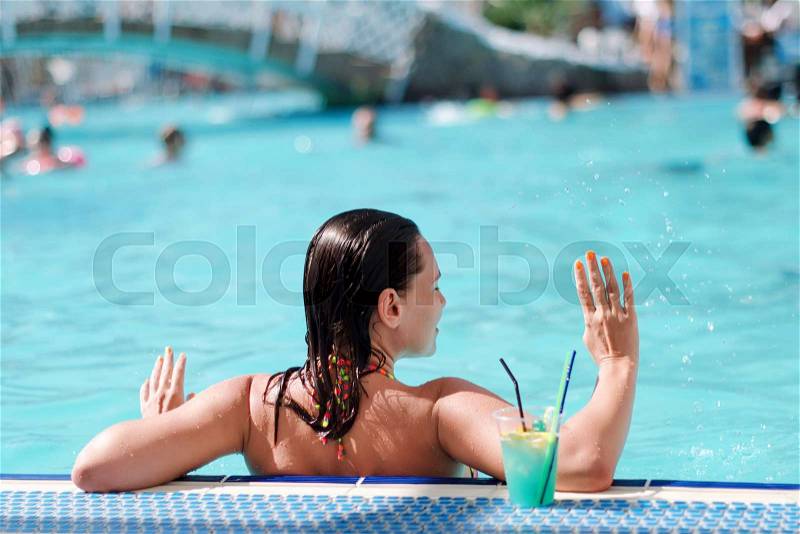Happy young woman in swimming pool drinking cocktail. Summer vacation in resort by the poolside. Active lifestyle, stock photo