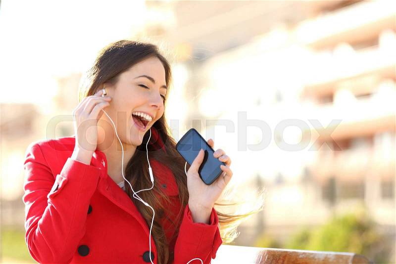 Funny girl listening to the music with earphones from a smart phone with an urban unfocused background, stock photo