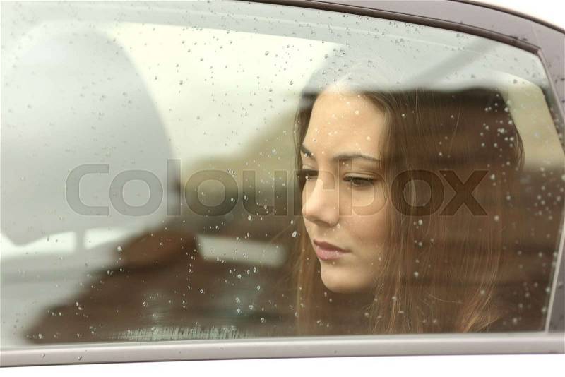 Sad woman looking down through a car window in a rainy day, stock photo