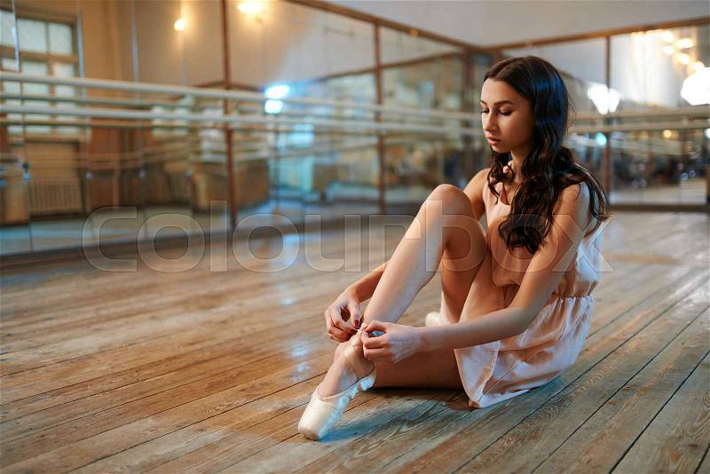Girl dancer sitting on the floor and corrects fasteners on shoes, stock photo