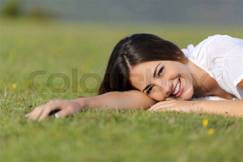Happy woman smiling and resting relaxed on the grass in the mountain or a park looking at camera, stock photo