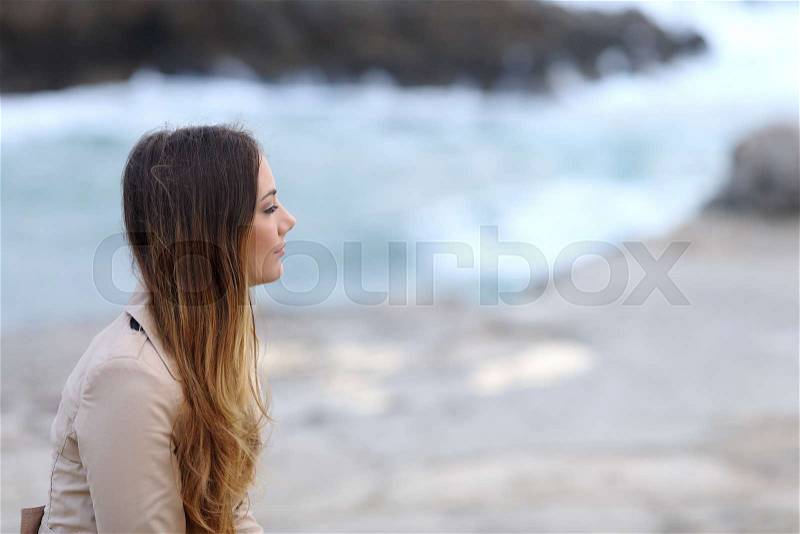 Profile of a serious pensive woman on the beach in winter looking away, stock photo