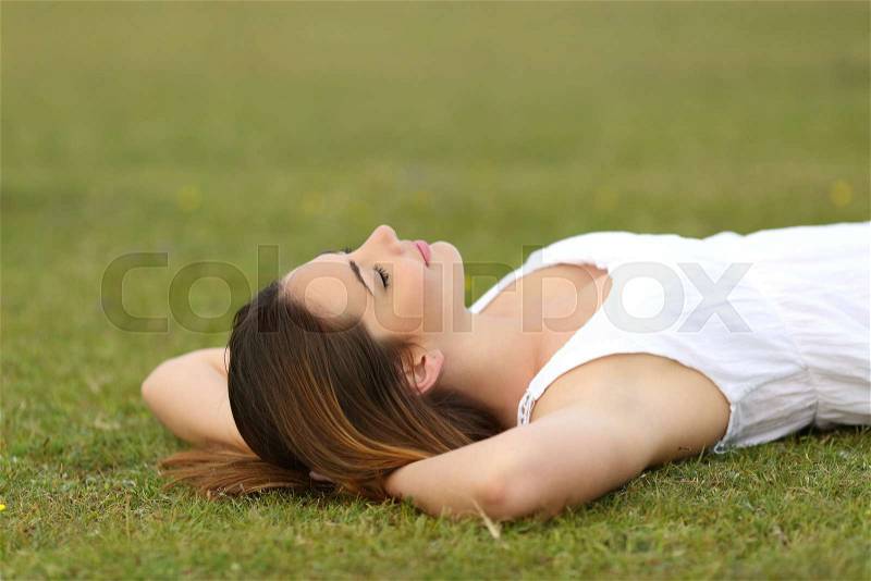 Relaxed woman lying on the grass sleeping in a tranquil scene with a green background, stock photo