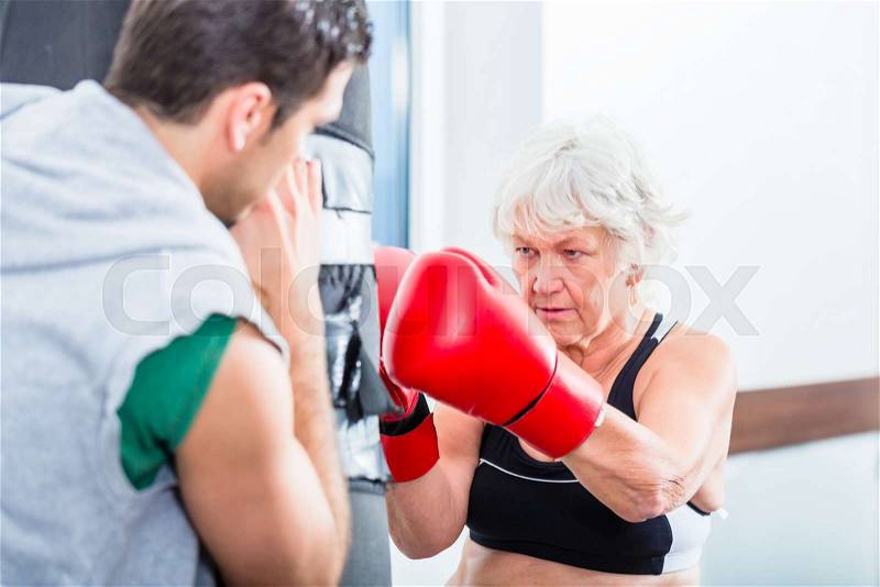 Senior woman with trainer in boxing sparring hitting sandbag, stock photo