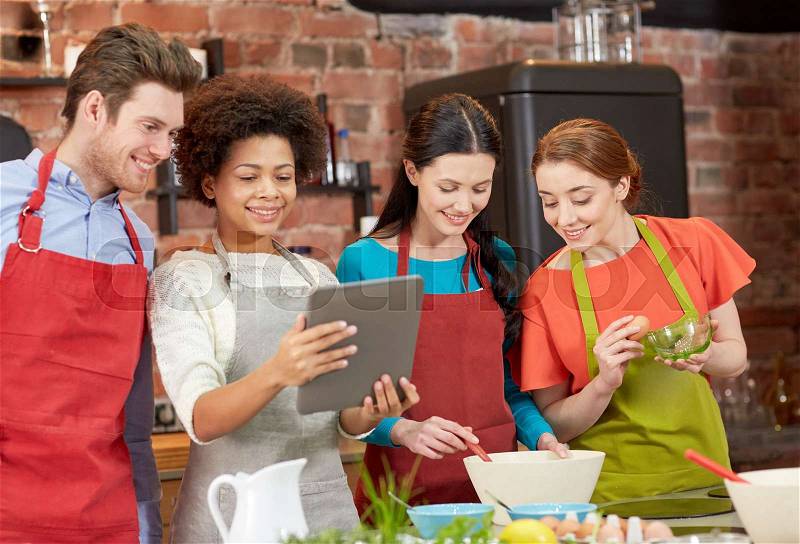 Cooking class, friendship, food, technology and people concept - happy friends with tablet pc computer in kitchen, stock photo