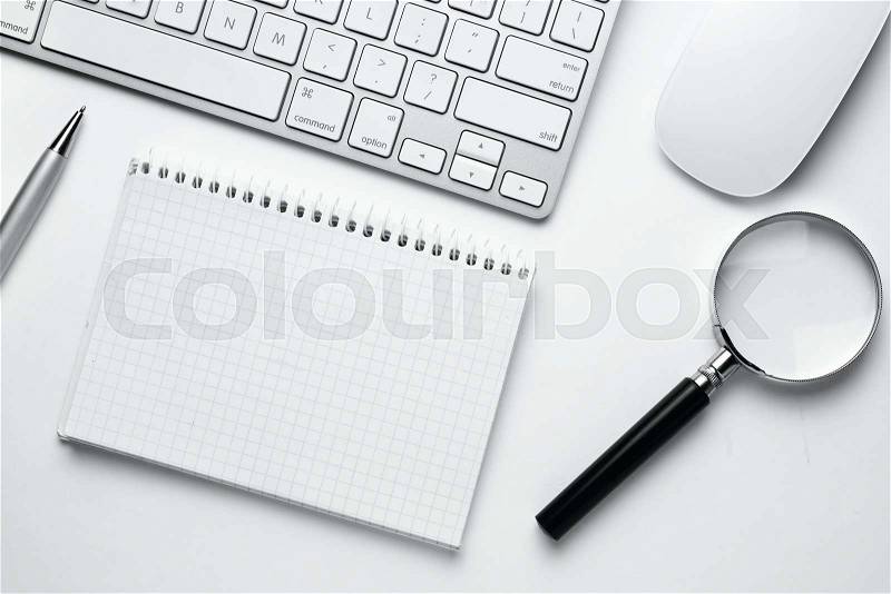 Conceptual White Office Stuffs with Magnifying Glass on Top of White Table, Emphasizing Copy Space on Clean Spiral Notebook with Grid Lines, stock photo