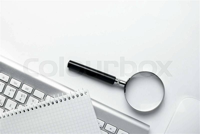 Conceptual image depicting conducting an online search for information with a magnifying glass on a blank notebook alongside a wireless computer mouse and keyboard, stock photo