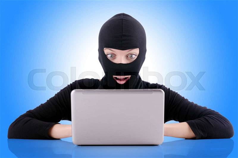 Hacker with computer wearing balaclava, stock photo