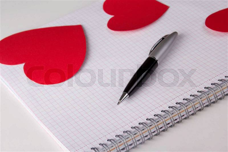 Note book with checked pages, pen and red paper hearts, stock photo