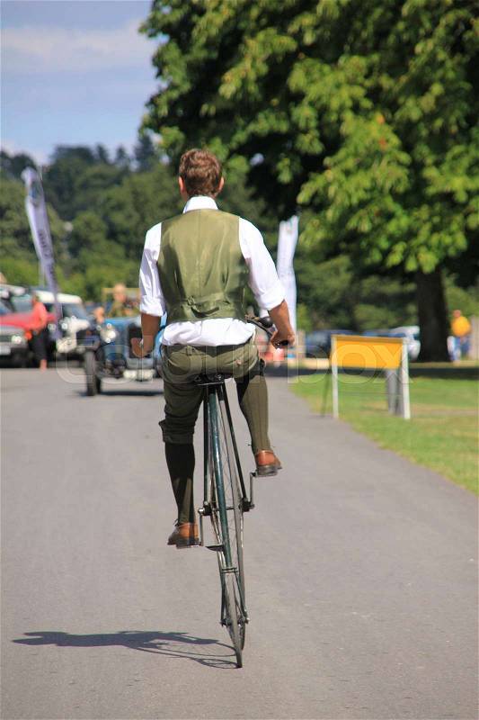 The gentleman in old suit shows the old velocipede on the road in Beaulieu in Hampshire in England in the summer, stock photo