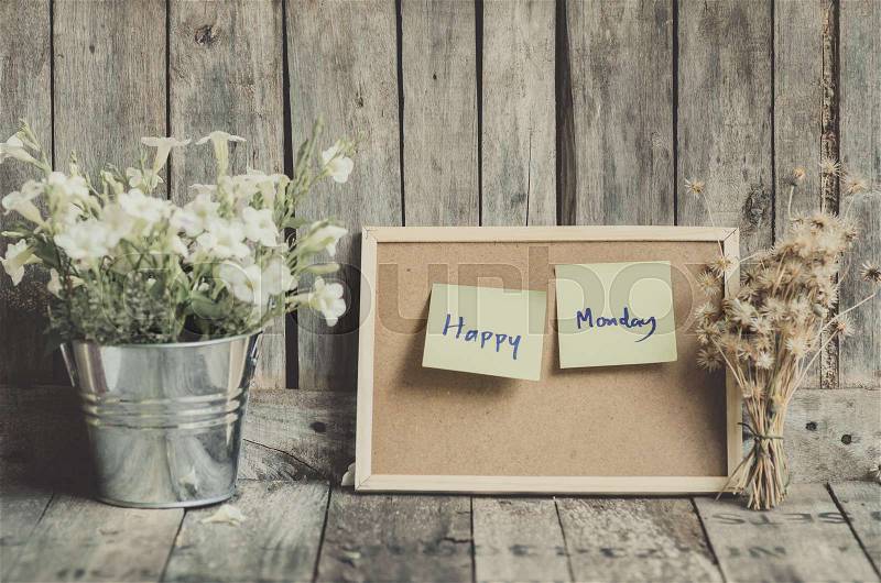 Vintage style effect Happy Monday message on corkboard with flowers by wooden background, stock photo