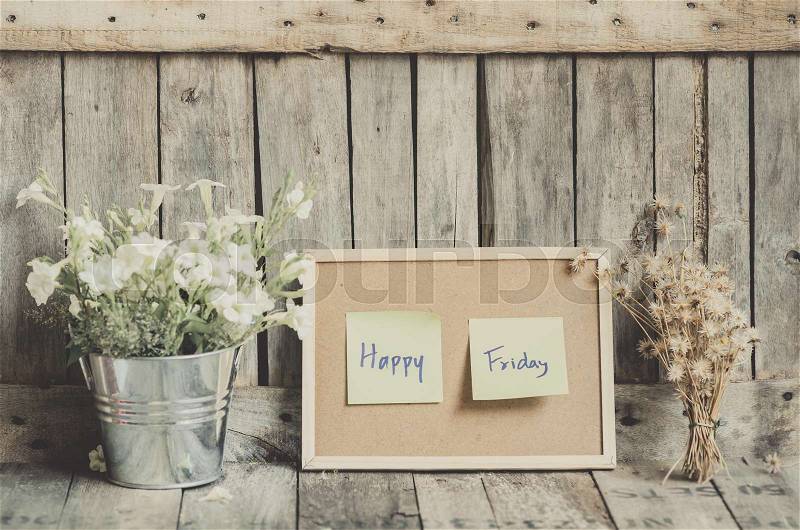 Vintage style effect Happy Friday message on corkboard with flowers by wooden background, stock photo