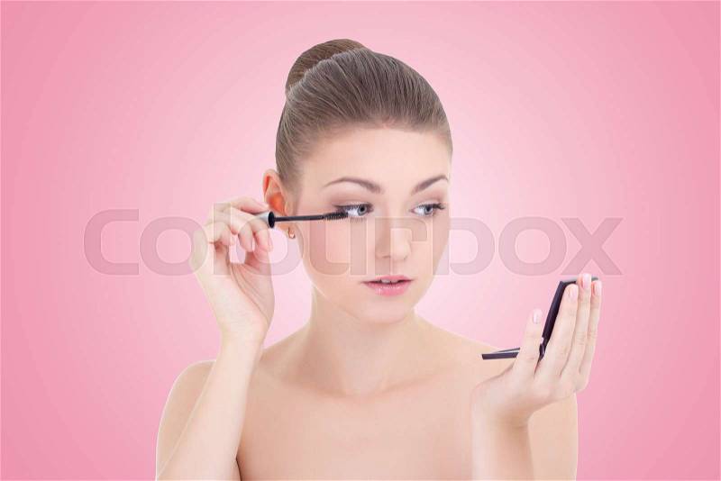 Portrait of young beautiful woman applying mascara on her eyelashes over pink background, stock photo