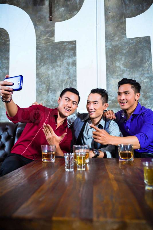 Asian party people group of young friends taking pictures or selfies with their mobile or cell phone in fancy night club, stock photo