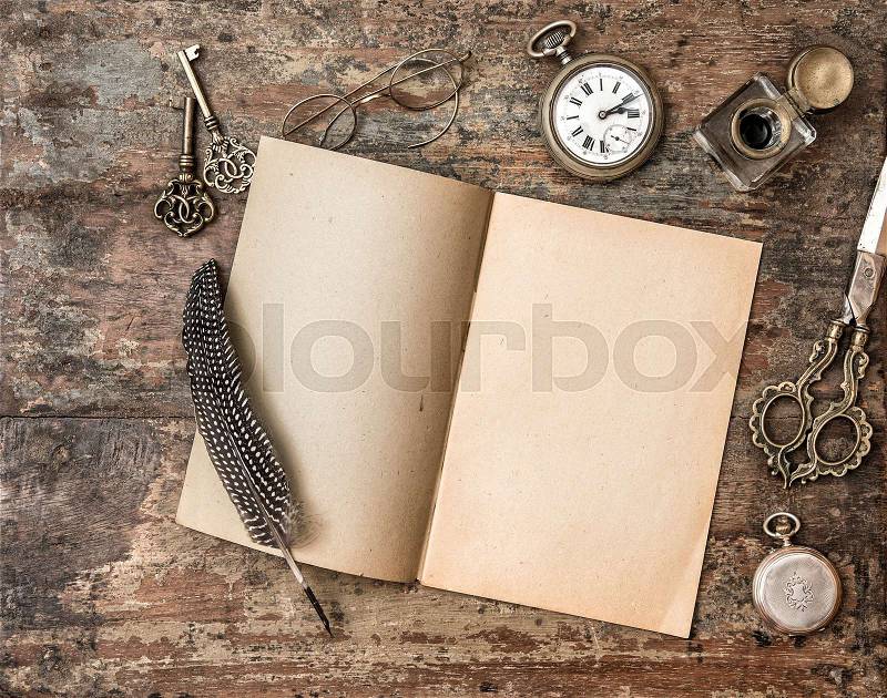 Open book and vintage writing on wooden table. Feather pen, inkwell, keys on textured background, stock photo