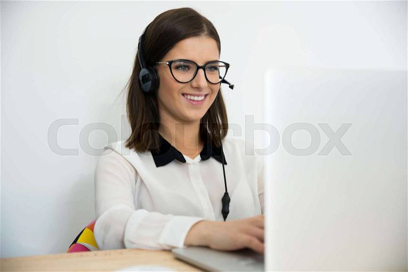 Happy female support operator in headset working on the laptop, stock photo