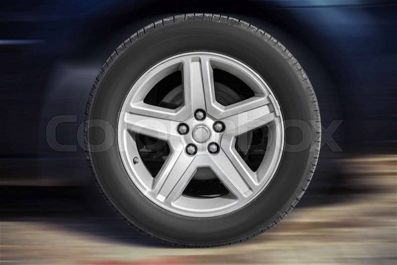 Modern automotive wheel on light alloy disc with blurred car background, stock photo