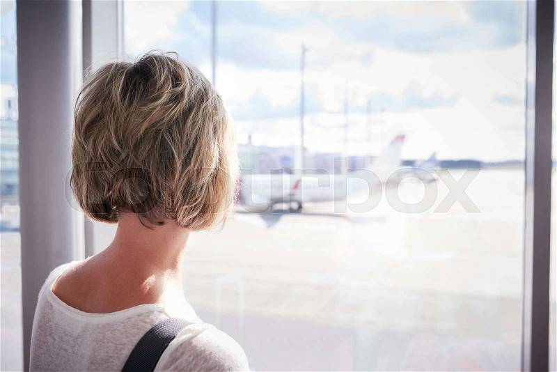 Closeup of a woman at the airport window looking to the airplane, stock photo