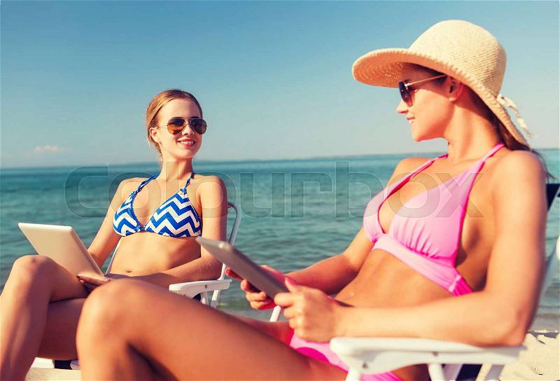 Summer vacation, travel, technology and people concept - smiling women with tablet pc computers sunbathing in lounge on beach, stock photo