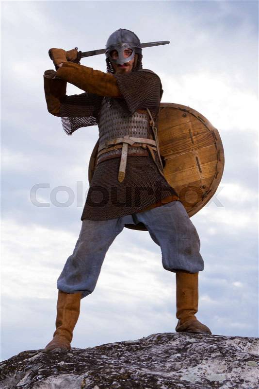 Knight on a rock with a sword against blue cloudy sky, stock photo