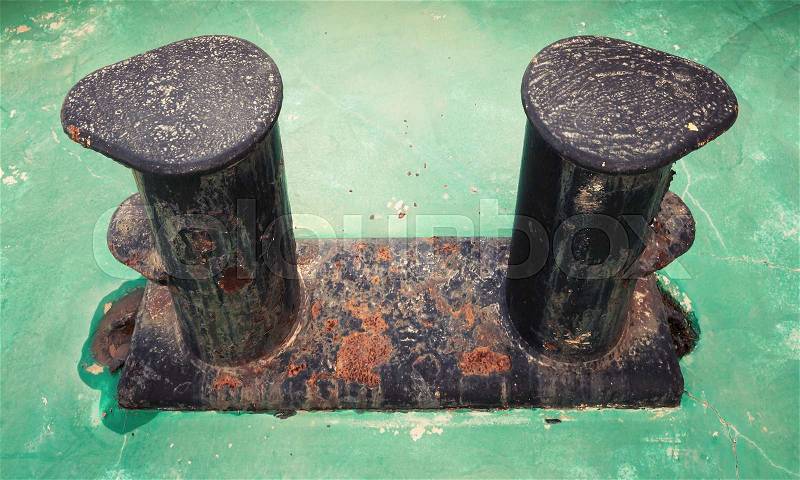 Old black rusted bollard mounted on green ship deck, stock photo