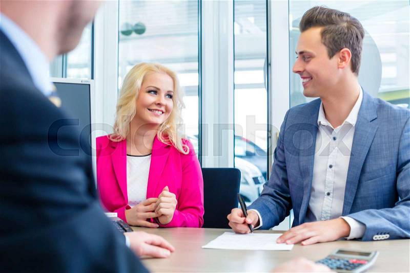 Couple buying car at dealership and signing sales contract with salesman, stock photo