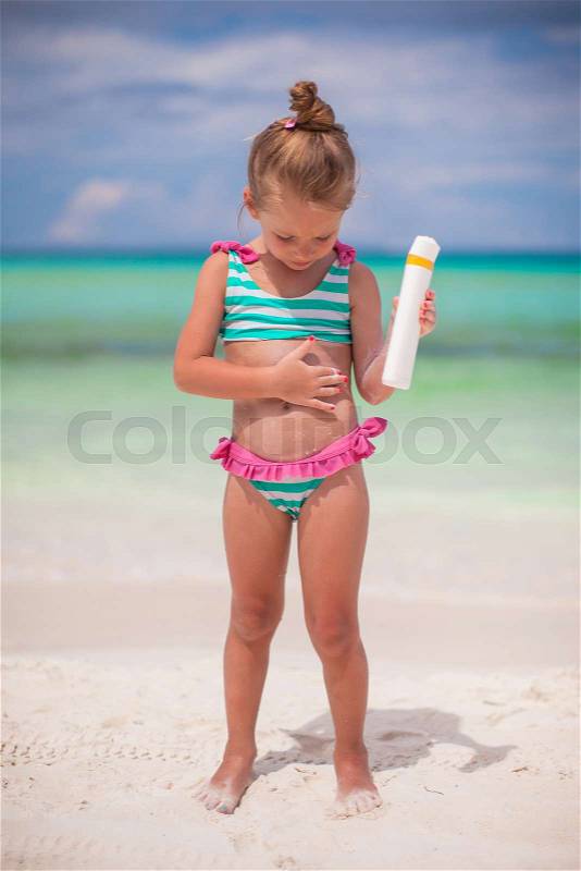 Little adorable girl in swimsuit holds suntan lotion bottle, stock photo