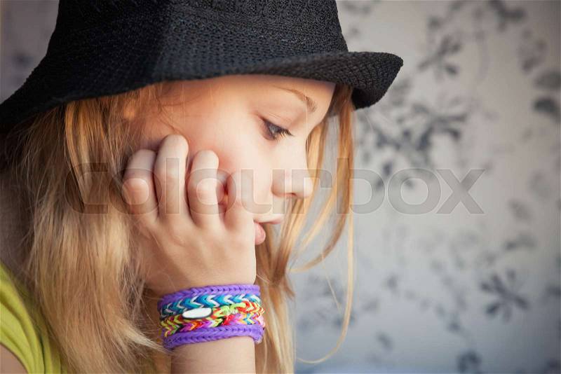 Profile portrait of beautiful blond teenage girl in black hat and rubber loom bracelets, toned photo, instagram style effect, stock photo