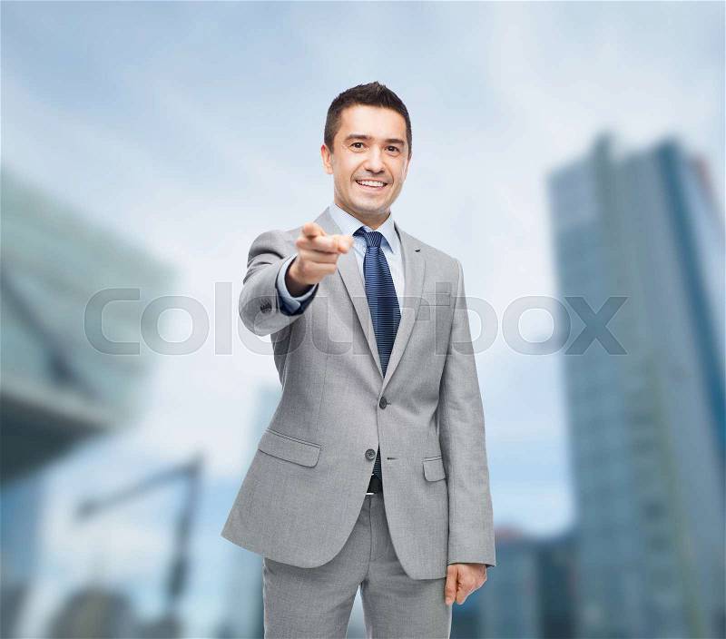 Business, people and office concept - happy smiling businessman in suit pointing at you over city background, stock photo