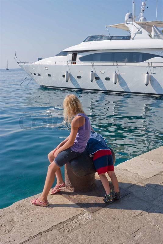 Brother and sister by the Adriatic sea looking at a huge yacht - Cavtat, Croatia, stock photo