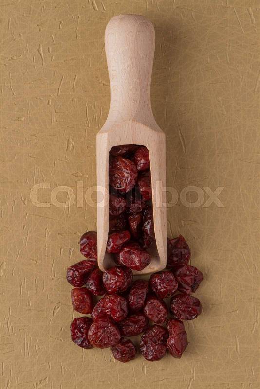 Top view of wooden scoop with dried cranberries against yellow vinyl background, stock photo