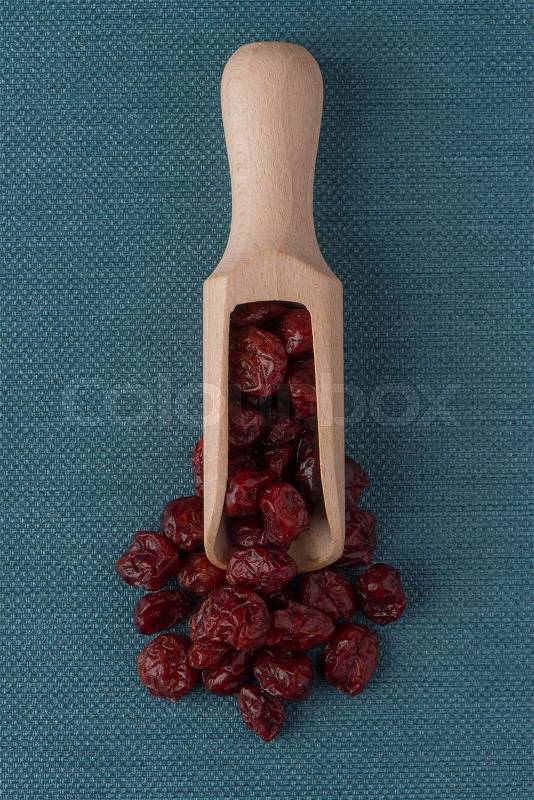Top view of wooden scoop with dried cranberries against blue vinyl background, stock photo