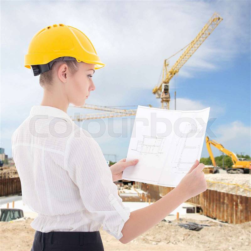 Business woman architect in yellow builder helmet with building plan at construction site, stock photo