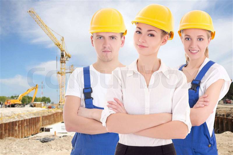 Team work concept - two young women and man in blue builder \'s uniform at construction site, stock photo