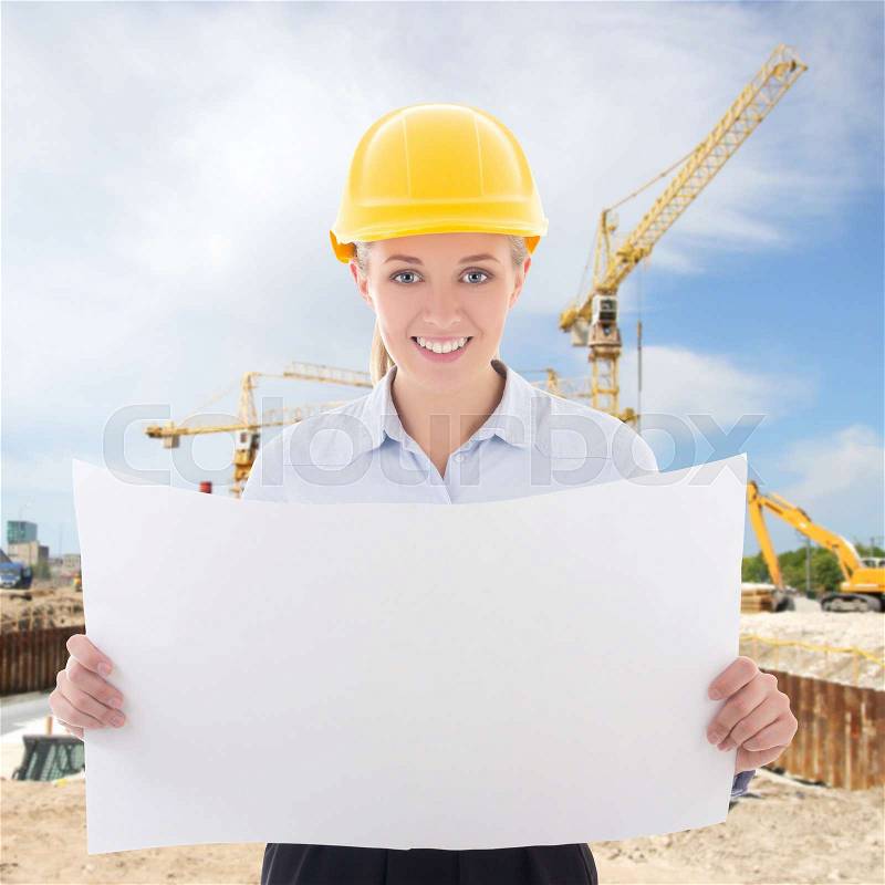 Happy business woman architect in yellow builder helmet holding building plan at construction site, stock photo